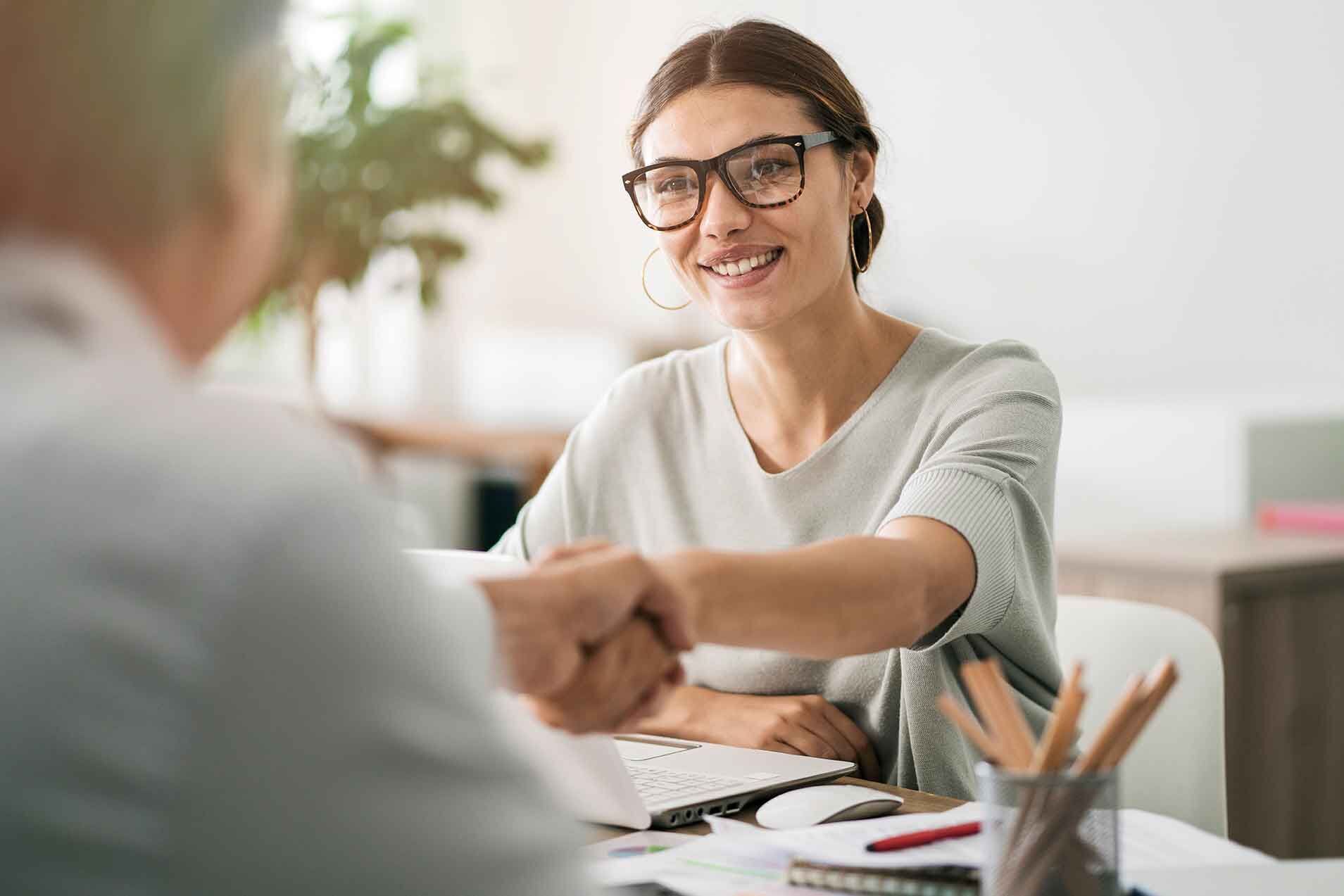 Eine Frau schüttelt dem Mann ihr gegenüber die Hand am Schreibtisch